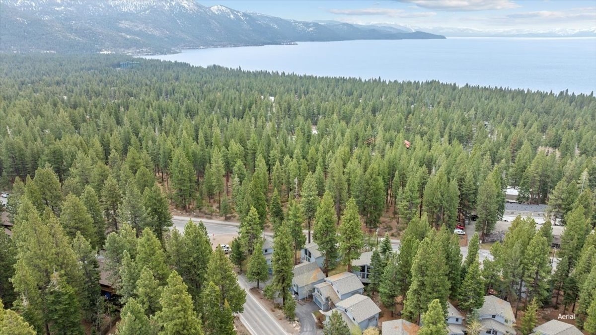 Aerial view over central Incline Village, with townhomes and condominiums among tall pines and Lake Tahoe and snow-capped mountains beyond