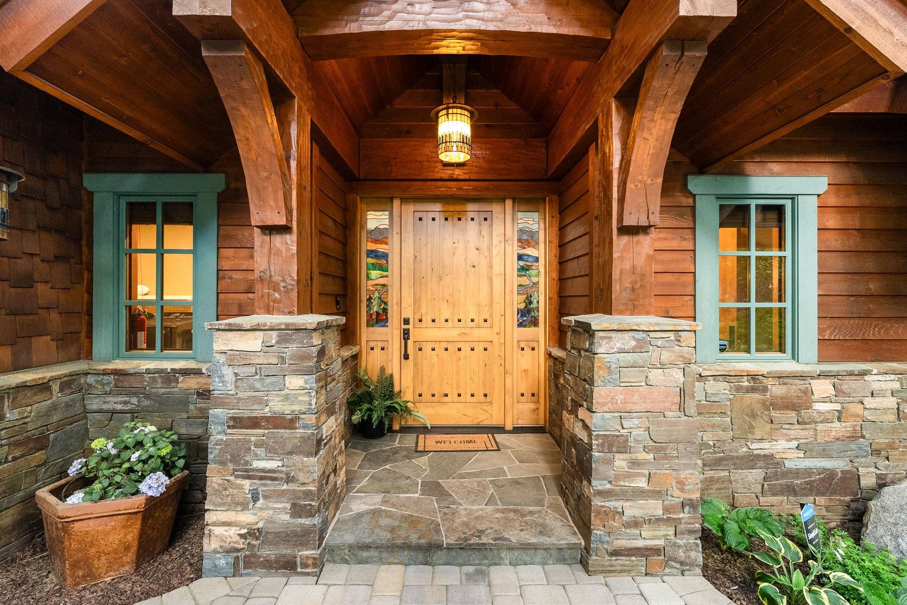 The timber-framed front entry of a mountain craftsman home in Incline Village, with a knotty-alder door, stained-glass sidelights, and stacked-stone pillars