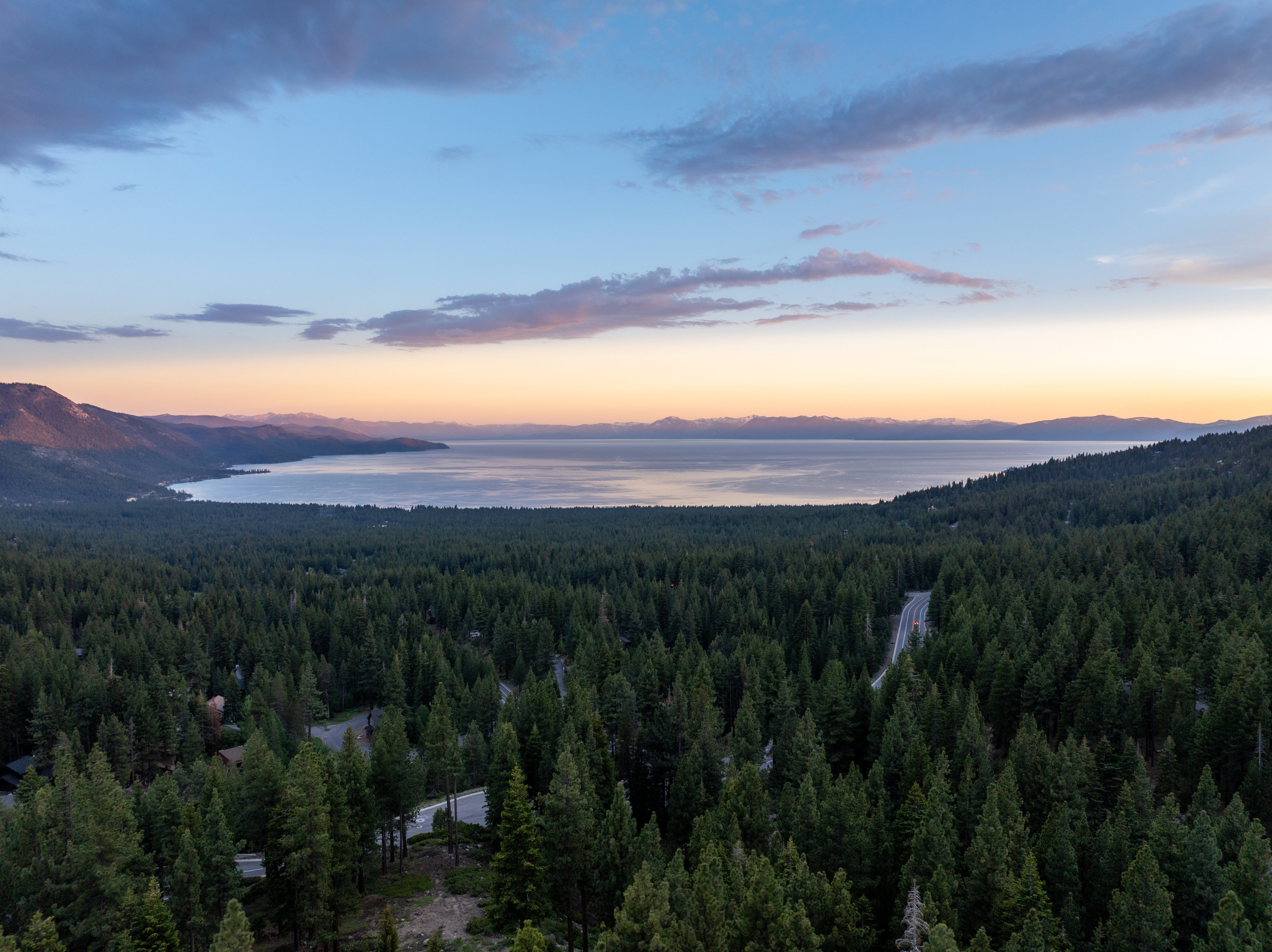 Aerial dusk view over Lake Tahoe's North Shore near Incline Village, Nevada, with forested hillsides and the Sierra Nevada mountains beyond