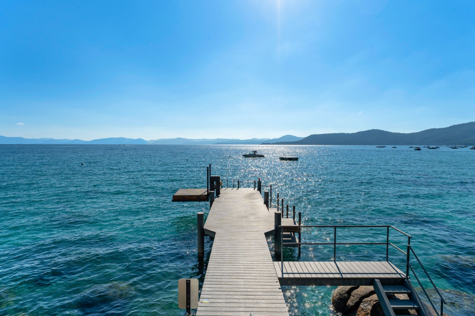 A private pier with a boat lift extending into Lake Tahoe's clear turquoise water, with moored boats and buoys offshore
