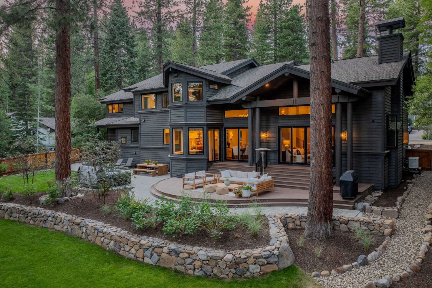 Modern mountain home in Incline Village with a twilight sky, forested lot, and stone-terraced deck